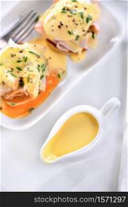 Hollandaise butter sauce in a gravy boat for breakfast served with Eggs Benedict- fried English bun, ham, poached eggs,