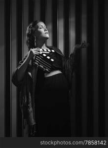 Hollywood black and white, a beautiful pregnant woman and she holds a clapboard - minimal lighting and strong contrast