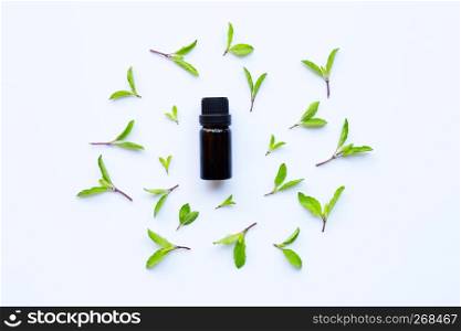Holy basil essential oil in a glass bottle with fresh holy basil leaves and flower
