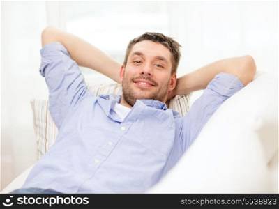 home and happiness concept - smiling man lying on sofa at home