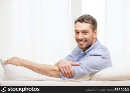 home and happiness concept - smiling man sitting on sofa at home