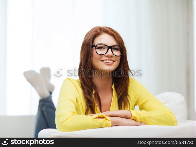home and happiness concept - smiling young woman in eyeglasses lying on sofa at home