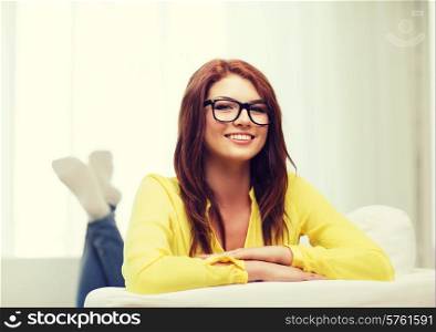 home and happiness concept - smiling young woman in eyeglasses lying on sofa at home