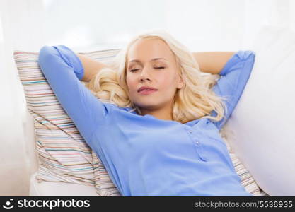 home and happiness concept - smiling young woman lying on sofa at home