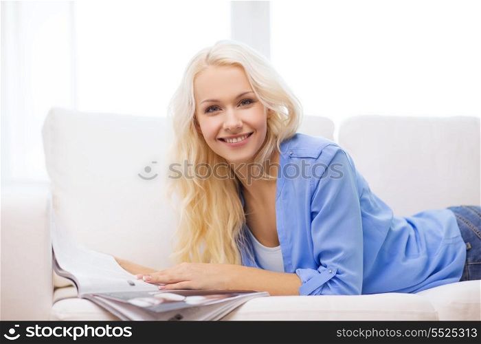 home and leasure concept - smiling woman lying on couch and reading magazine at home