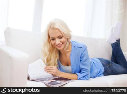 home and leasure concept - smiling woman lying on couch and reading magazine at home