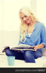 home and leasure concept - smiling woman sitting on couch and reading magazine at home