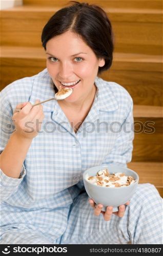 Home breakfast happy woman in pajamas eating cereals on stairs