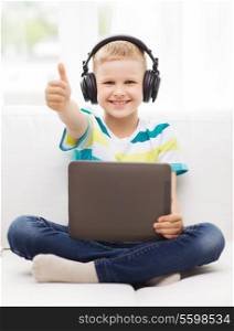 home, childhood, leisure, technology and music concept - smiling little boy with tablet pc computer and headphones showing thumbs up at home
