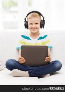 home, childhood, leisure, technology and music concept - smiling little boy with tablet pc computer and headphones at home
