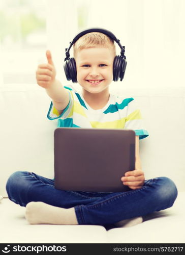 home, childhood, leisure, technology and music concept - smiling little boy with tablet pc computer and headphones showing thumbs up at home