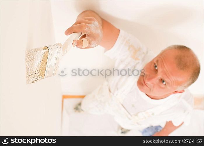 Home decorating mature man painting white wall with paint brush