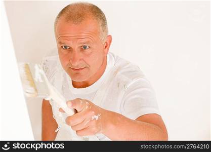 Home decorating mature man painting white wall with paint brush