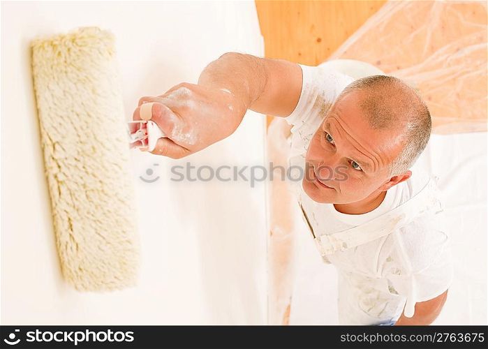 Home decorating mature man painting white wall with paint roller