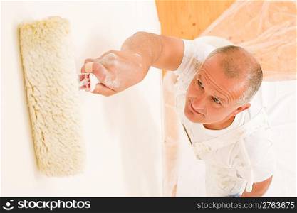 Home decorating mature man painting white wall with paint roller