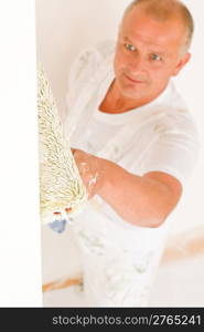 Home decorating mature man painting white wall with paint roller