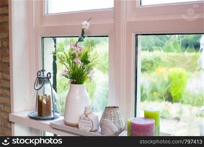 home decoration on windowsill with colorful flowers and white vase and candles on a sunny day. home decoration on windowsill with colorful flowers and white vase on a sunny day