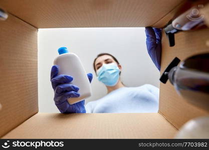 home delivery, shipping and pandemic concept - woman in protective medical mask and gloves unpacking parcel box with cosmetics and beauty products. woman in mask unpacking parcel box with cosmetics