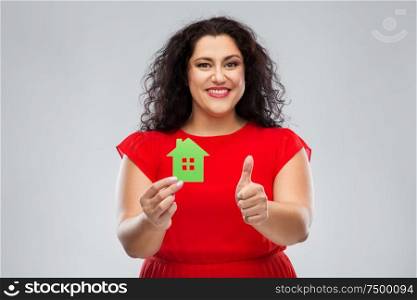 home, ecology and environmentally friendly concept - happy woman in red dress holding green house icon and showing thumbs up over grey background. woman holding green house and showing thumbs up