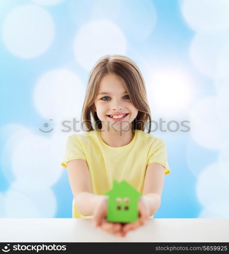 home, education, happiness, childhood and people concept - beautiful little girl sitting at table holding white house cutout over blue background