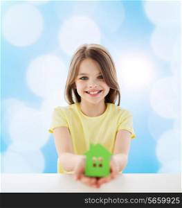home, education, happiness, childhood and people concept - beautiful little girl sitting at table holding white house cutout over blue background