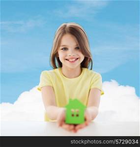 home, education, happiness, childhood and people concept - beautiful little girl sitting at table holding white house cutout over blue sky background