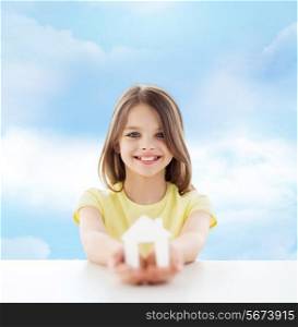 home, education, happiness, childhood and people concept - smiling little girl holding green house cutout over cloudy sky background