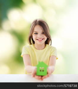 home, education, nature, childhood and people concept - beautiful little girl sitting at table holding white house cutout over green background