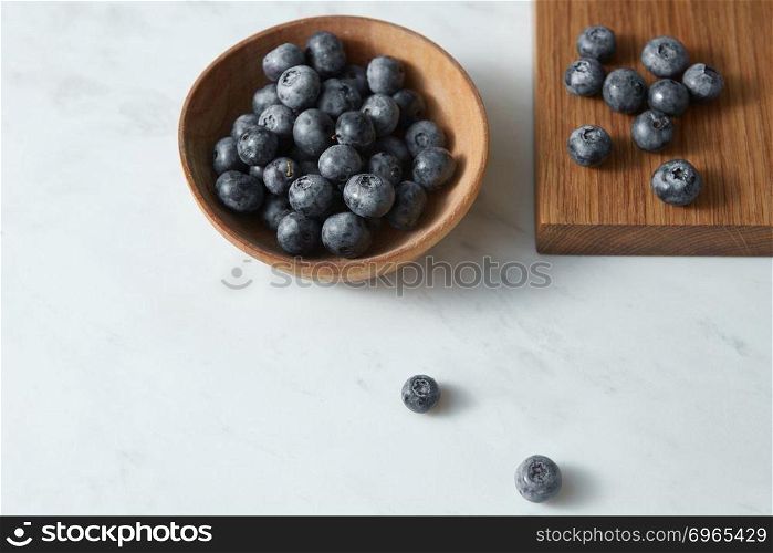 Home grown natural fresh berries for cooking sweet desserts on kitchen table. Concept of healthy homemade food.. Summer organic natural sweet blueberries in a wooden plate on a white. Copy space.