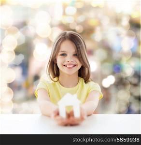 home, happiness, childhood and people concept - beautiful little girl sitting at table holding white house cutout over sparkling background