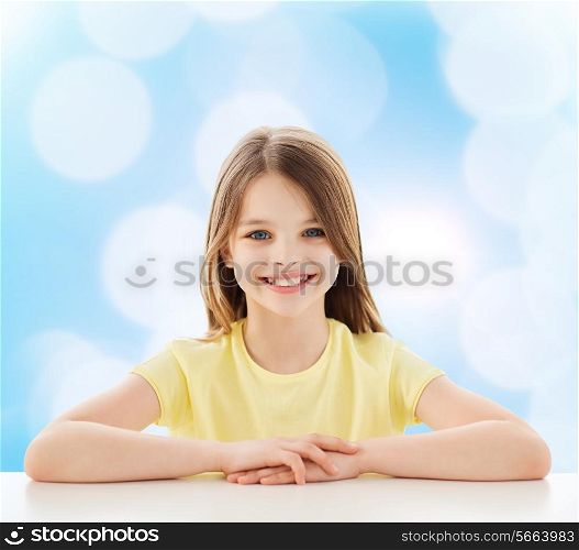 home, happiness, childhood and people concept - beautiful little girl sitting at table over blue background
