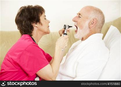 Home health care nurse uses an otoscope and tongue depressor to look in a patient&rsquo;s mouth.