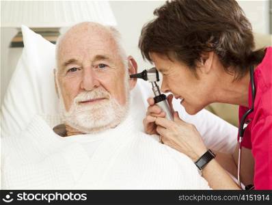 Home health nurse checking her senior patient&rsquo;s ears with an otoscope.