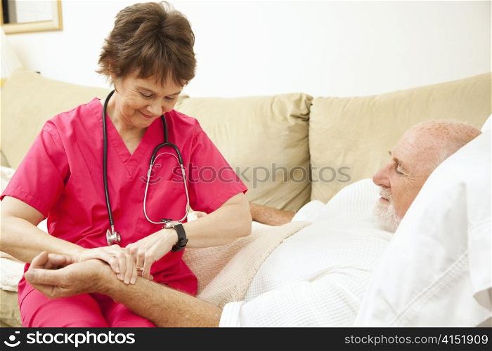 Home health nurse taking the pulse of an elderly, home-bound patient.