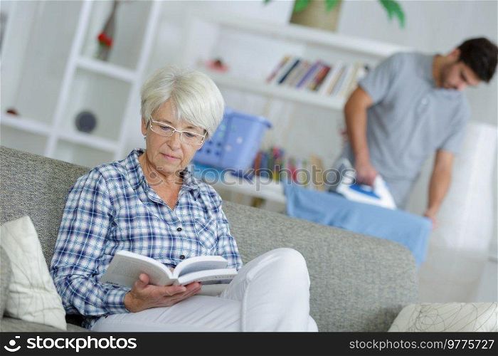 home help man ironing and senior lady reading a book