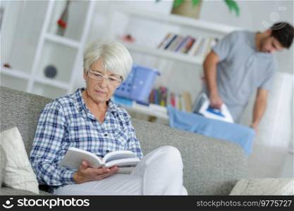 home help man ironing and senior lady reading a book