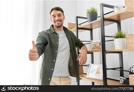 home improvement and decoration and people concept - happy smiling man standing at shelf and showing thumbs up. smiling man showing thumbs up at home