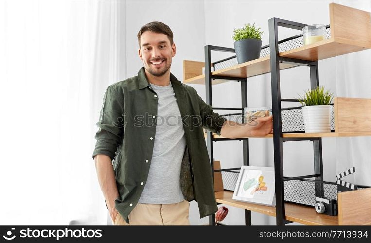 home improvement and decoration and people concept - happy smiling man standing at shelf. happy smiling man standing at shelf at home
