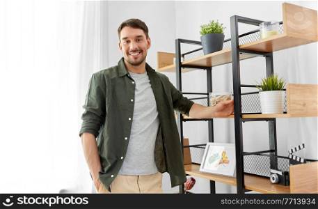 home improvement and decoration and people concept - happy smiling man standing at shelf. happy smiling man standing at shelf at home
