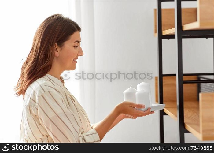 home improvement and decoration and people concept - happy smiling woman placing candles to shelf. woman decorating home with candles