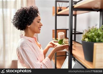 home improvement and decoration and people concept - happy smiling young woman placing candles with eucalyptus branch to shelf. happy woman decorating home with candles