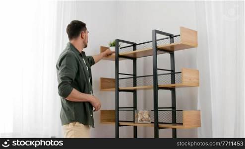 home improvement and decoration and people concept - man arranging shelf with flower in pot. man decorating home and arranging shelf