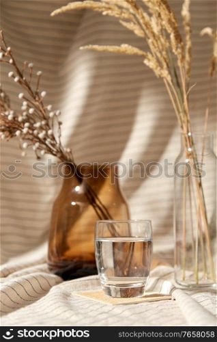 home improvement and decoration concept - still life of water in glass, decorative dried flowers in vase and bottle over drapery. glass of water, decorative dried flowers in vases