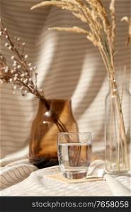 home improvement and decoration concept - still life of water in glass, decorative dried flowers in vase and bottle over drapery. glass of water, decorative dried flowers in vases