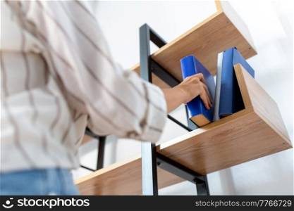 home improvement and people concept - close up of woman arranging books on shelving. woman arranging books on shelving at home