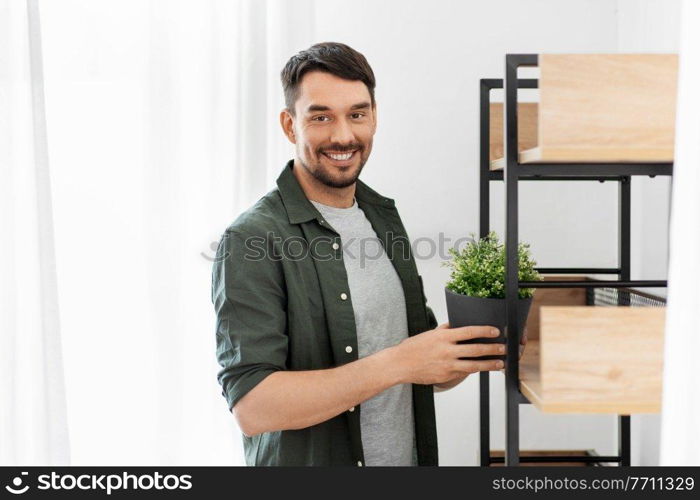 home improvement, decoration and people concept - happy smiling man placing flower in pot or houseplant to shelf. man decorating home with flower or houseplant