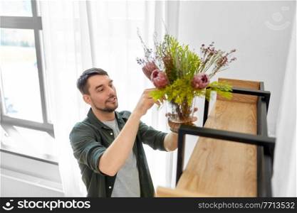 home improvement, decoration and people concept - happy smiling man placing flowers in vase to shelf. man decorating home with flowers in vase