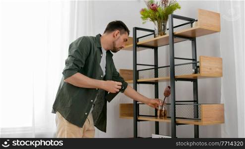 home improvement, decoration and people concept - happy smiling man placing flowers in vase to shelf. man decorating home with flowers in vase