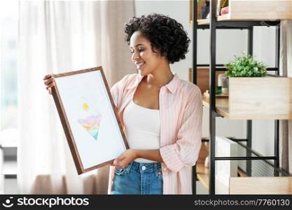 home improvement, decoration and people concept - happy smiling woman holding abstract watercolor picture in frame at shelf. happy woman holding picture in frame at home