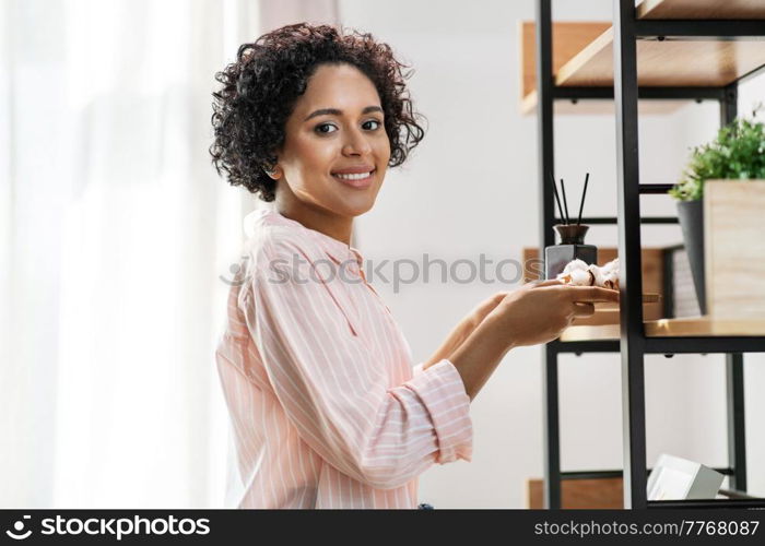 home improvement, decoration and people concept - happy smiling woman holding board with aroma reed diffuser and cotton flower at shelf. woman with aroma reed diffuser and cotton at home